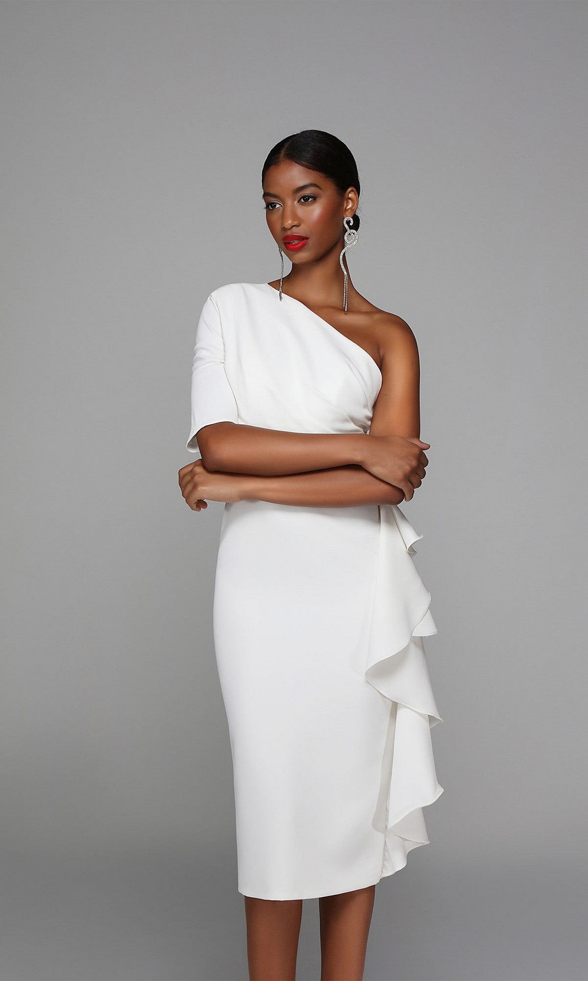Woman in a knee length semi-formal Alyce 70006 dress with ruffle detailing and one-shoulder design, standing with arms crossed against a plain gray background.